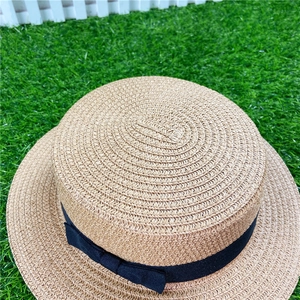 Top view of natural straw flat top sun hat with black bow on green artificial grass