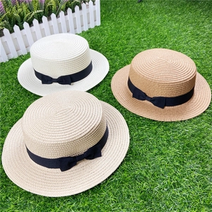 Flat top straw boater hats in three colors with black bow ribbons on a grass lawn