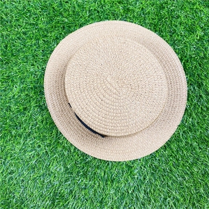 Top view of a classic woven boater hat with black ribbon on a green grass background