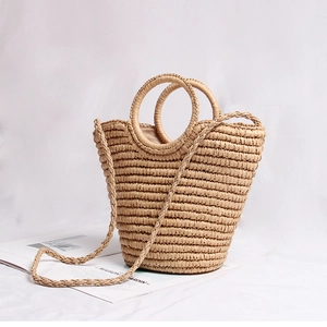 Detailed view of handmade straw handbag with round handles and woven strap on white fabric