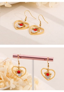 Details von goldenen Herzohrringen mit Astronauten-Motiv und roten sowie weißen Kristallen