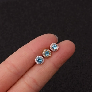 Macro view of colorful zircon screw earrings in silver, gold, and rose gold on a finger