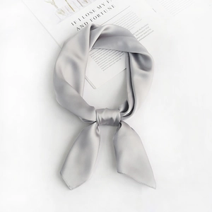 Detail of soft grey square silk scarf tied in a knot on a white background with a book