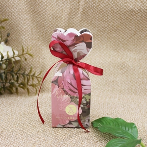 Close-up of pink floral candy gift box with red ribbon bow on a natural burlap background