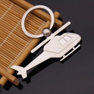 Close-up of a silver metal helicopter keychain on a natural bamboo and dark reflective surface