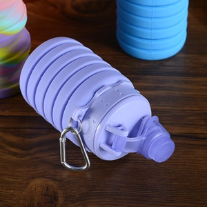 Close-up of a purple collapsible silicone sports bottle with metal carabiner on wood