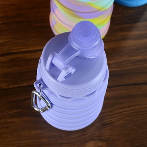 Detail of a purple collapsible silicone water bottle with a metal hook on a wooden table