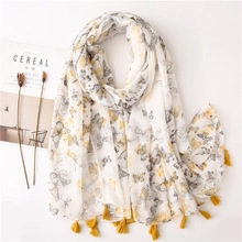 Detail of white cotton scarf with yellow butterfly pattern and fringed edges on a desk