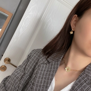 Detail of a minimalist gold flower chain necklace and heart earrings on a grey suit model