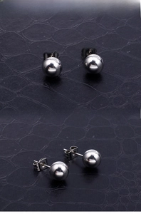 Detailed close-up of classic polished stainless steel ball stud earrings on black texture