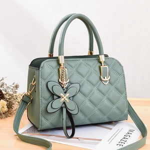 Elegant light green quilted crossbody bag with golden butterfly charm on a wooden table