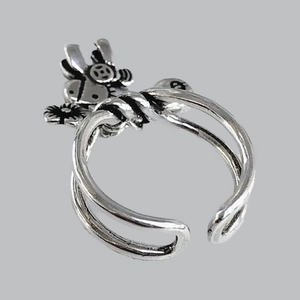 Detail view of silver open ring with decorative bow and coin motifs on light gray surface