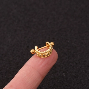 Macro shot of a tiny gold U-shaped ear stud with zircon flower on a fingertip