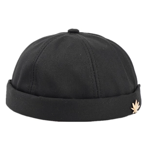 Black cotton docker cap with golden maple leaf metal emblem in a retro streetwear style