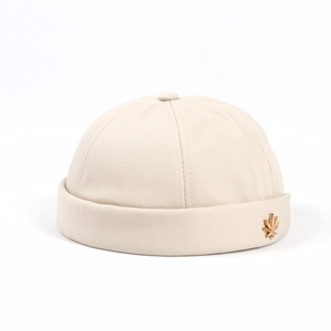 Detail of beige cotton docker hat with a decorative gold maple leaf metal pin