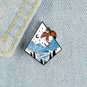Gros plan sur un pin's dragon émaillé avec motif de montagne et forêt sur denim bleu