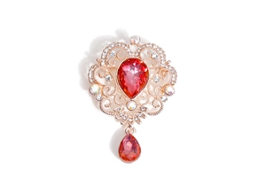 Macro detail of a golden baroque brooch featuring a red teardrop crystal and floral pattern