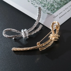 Gold and silver twisted knot bow brooches with intricate metal texture on black background
