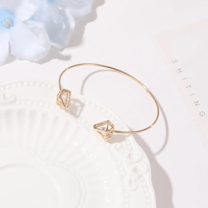 Detailed close-up of a gold hollow triangle bangle with zircon on a white plate
