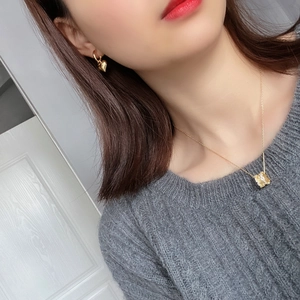 Detail of square hammered pendant necklace and gold heart earrings on a grey sweater