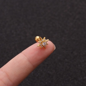 Close-up of gold star stud earring with white zircon inlay held between fingers