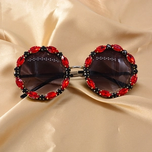 Detail of red crystal-embellished round sunglasses on elegant champagne silk fabric
