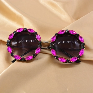 Detail of round sunglasses with vibrant rose pink rhinestones on a silk background