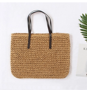 Detailed close-up of woven straw tote bag with brown leather handles and natural texture