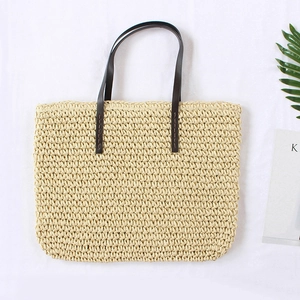 Top view of woven straw tote bag with brown leather handles on white background