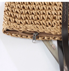 Close-up of natural straw weave texture with brown zipper and leather shoulder strap