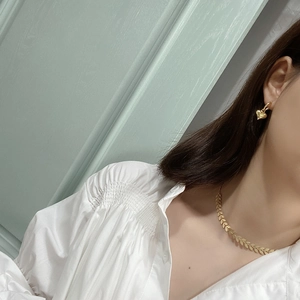 Close-up of golden leaf necklace and heart earring worn with a white pleated shirt