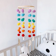 Detail of bohemian rainbow pom pom mobile with wooden feathers on a white baby crib