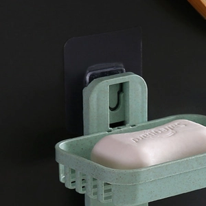 Detail of light green adhesive soap dish with drain holes on matte black background