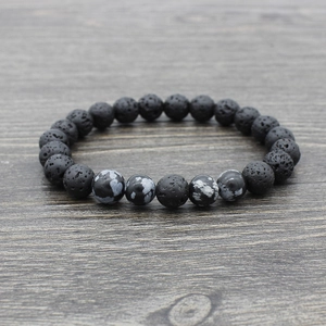 Detailed view of textured black lava rock and snowflake obsidian yoga beads on a wood surface