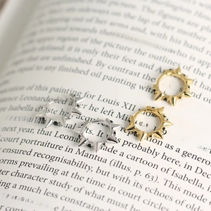 Close-up of gold and silver spike ear cuffs with black crystals on a vintage book