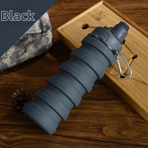 Close-up of a dark grey foldable silicone water bottle with a metal carabiner on a desk