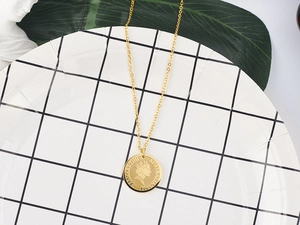 Detailed shot of 18K gold coin necklace featuring Queen Elizabeth II relief on white tile