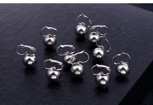 Macro view of silver spherical drop earrings with polished metallic finish on leather