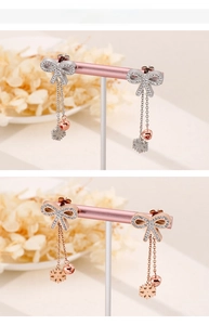 Detail of bow earrings with tassels, snowflake and bell charms in silver and rose gold