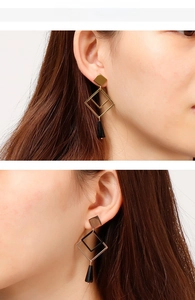 Close-up of geometric titanium earrings with gold square studs and black charms