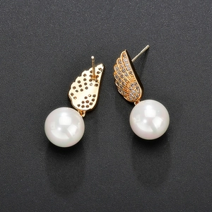 Detail of golden wing earrings with AAA cubic zirconia and white pearls on black background
