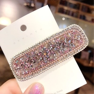 Dettaglio di un grande fermaglio rettangolare con strass rosa e lilla su carta bianca