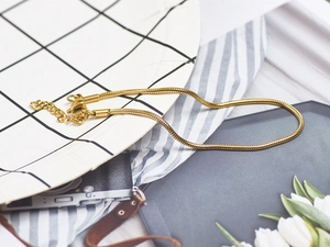 Detail of 18K gold plated snake chain bracelet with lobster clasp on vintage background
