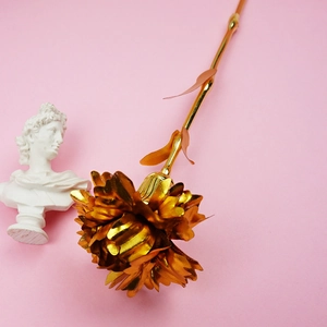 Detail shot of golden foil carnation flower against a pink background with small statue