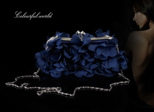 Close-up of navy blue floral evening clutch with silver chain on reflective surface