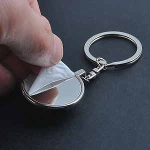 Close-up of peeling protective film from a round silver metal sports keyring mirror