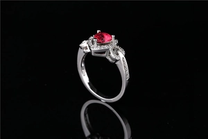 Macro view of a heart-shaped red gemstone ring with halo zircons on a black background
