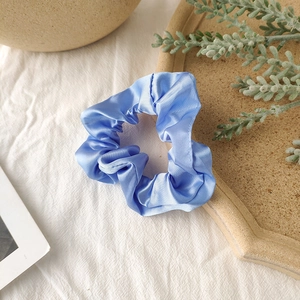 Detail of light blue satin scrunchie with silky texture on a decorative tray