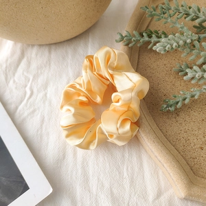 Close-up of champagne satin scrunchie with glossy texture on a white textured cloth