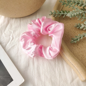 Close-up of pink satin scrunchie with silk texture and elegant pleats on ceramic tray
